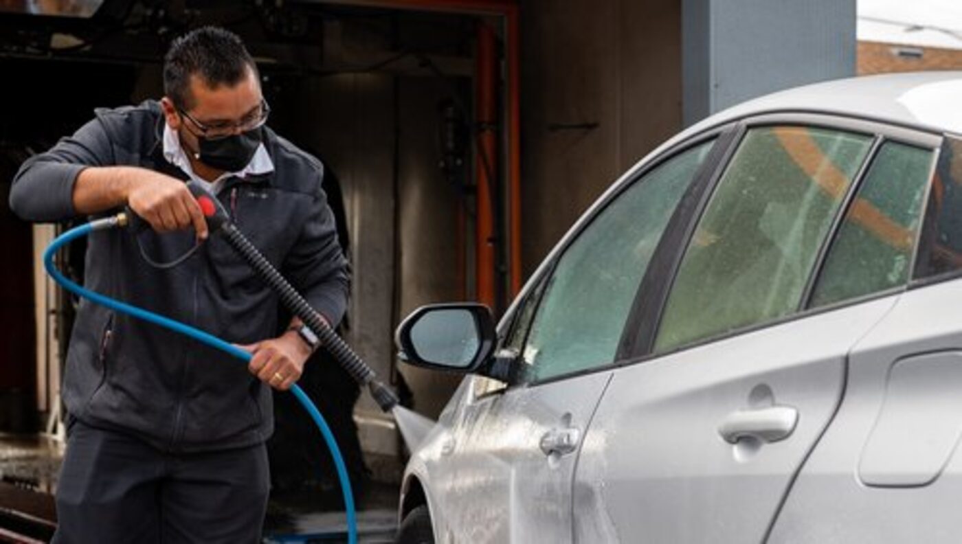 A Blue Star Xpress Wash team member hand-washing a silver sedan with a pressure washer in the detail bay